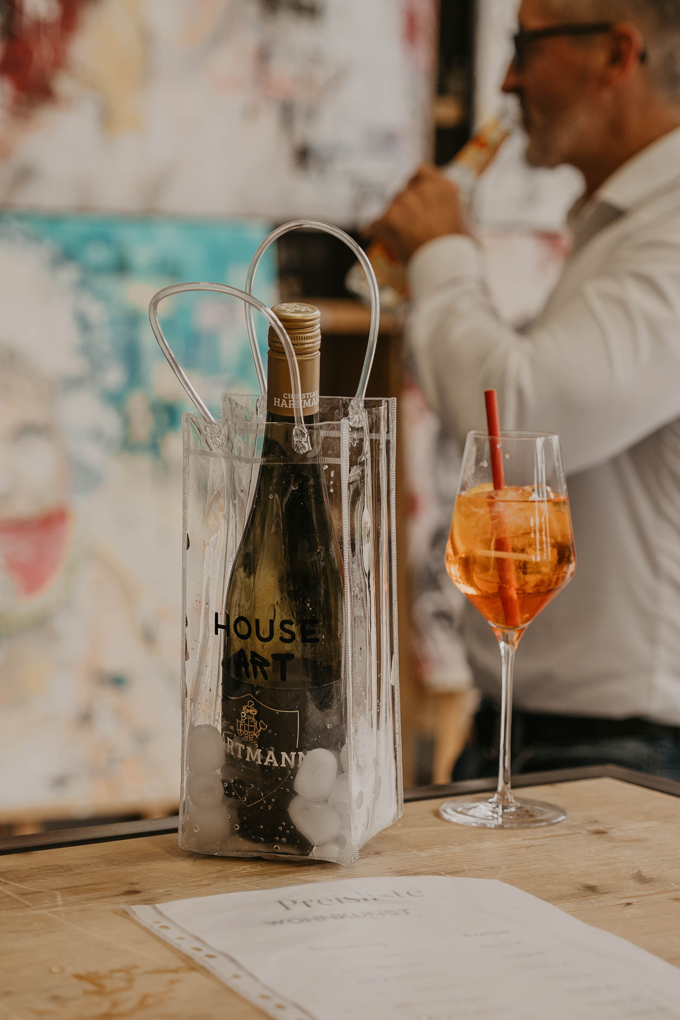 House Art Weinkühlbeutel mit Champagner und Aperol Spritz auf der Theke vor abstraktem Gemälde