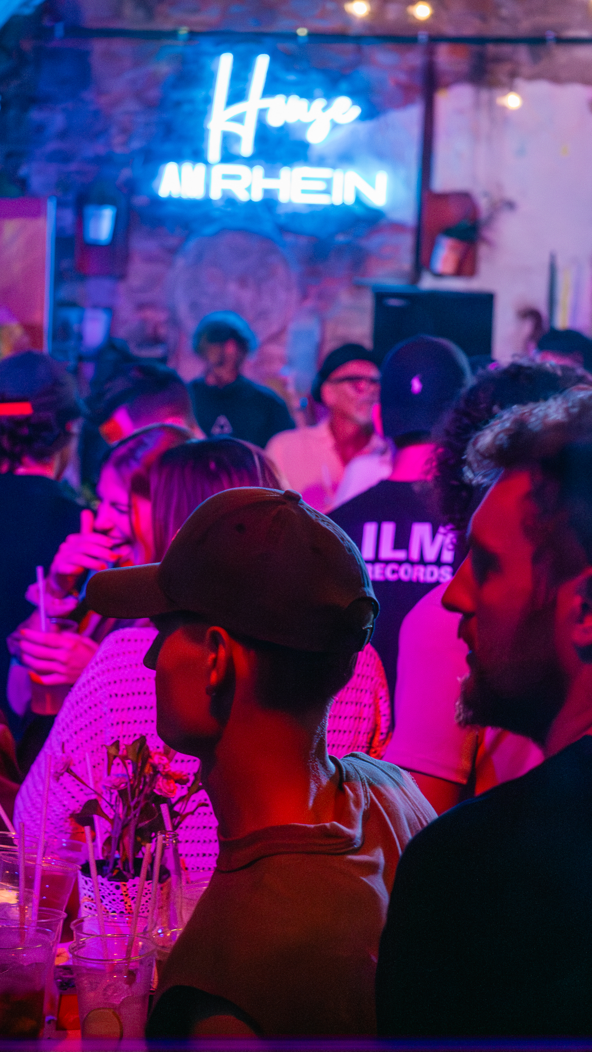 Gäste feiern unter dem House am Rhein Neonschild bei pinkfarbener Clubbeleuchtung