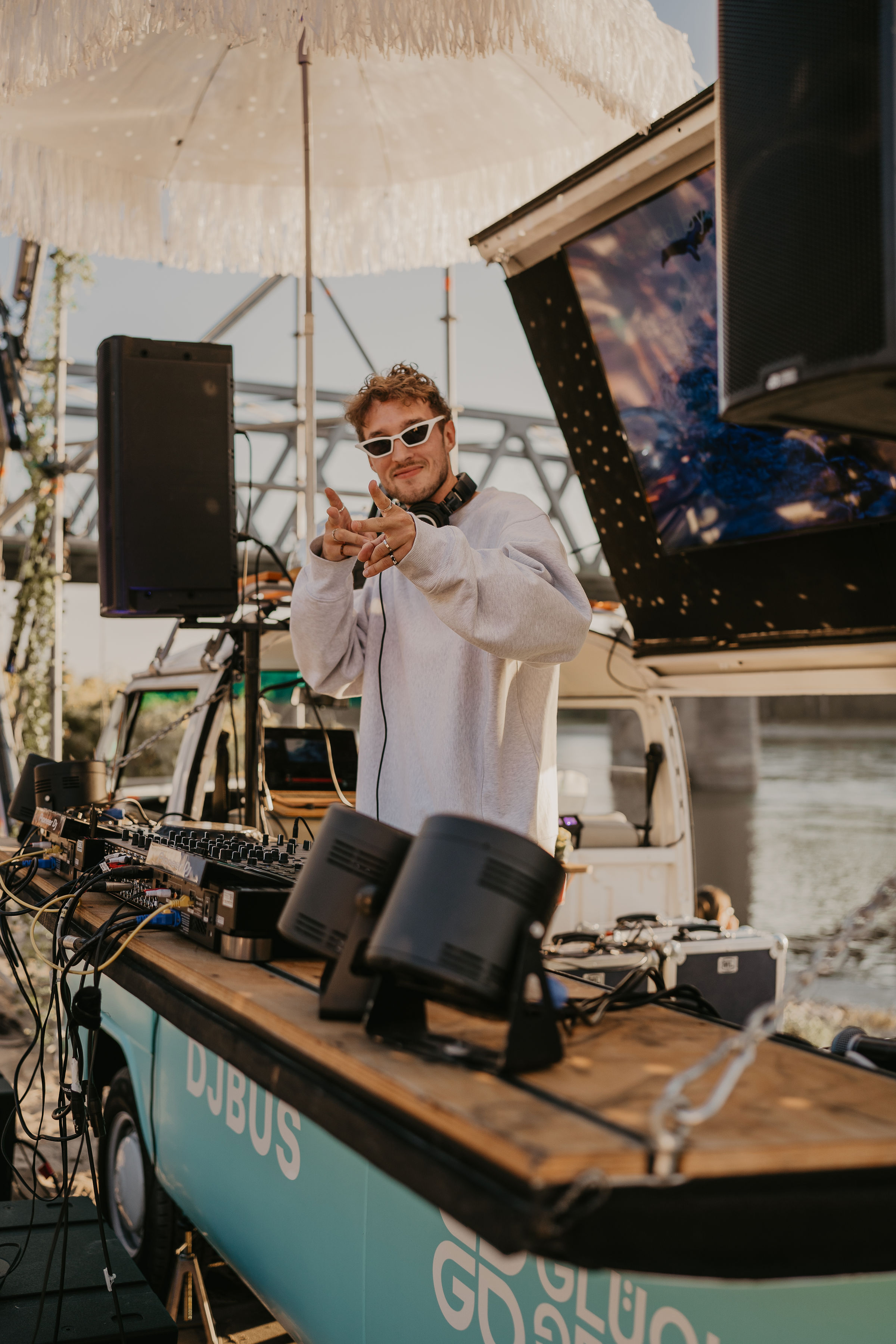 DJ im weißen Hoodie am DJ-Bus am Rheinufer zeigt in die Kamera