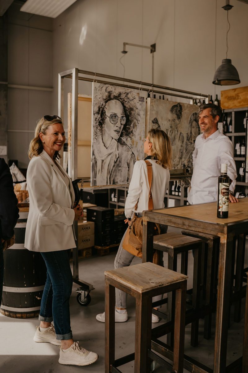 Gäste unterhalten sich lachend vor einem großen Porträtgemälde bei der House Art Vernissage