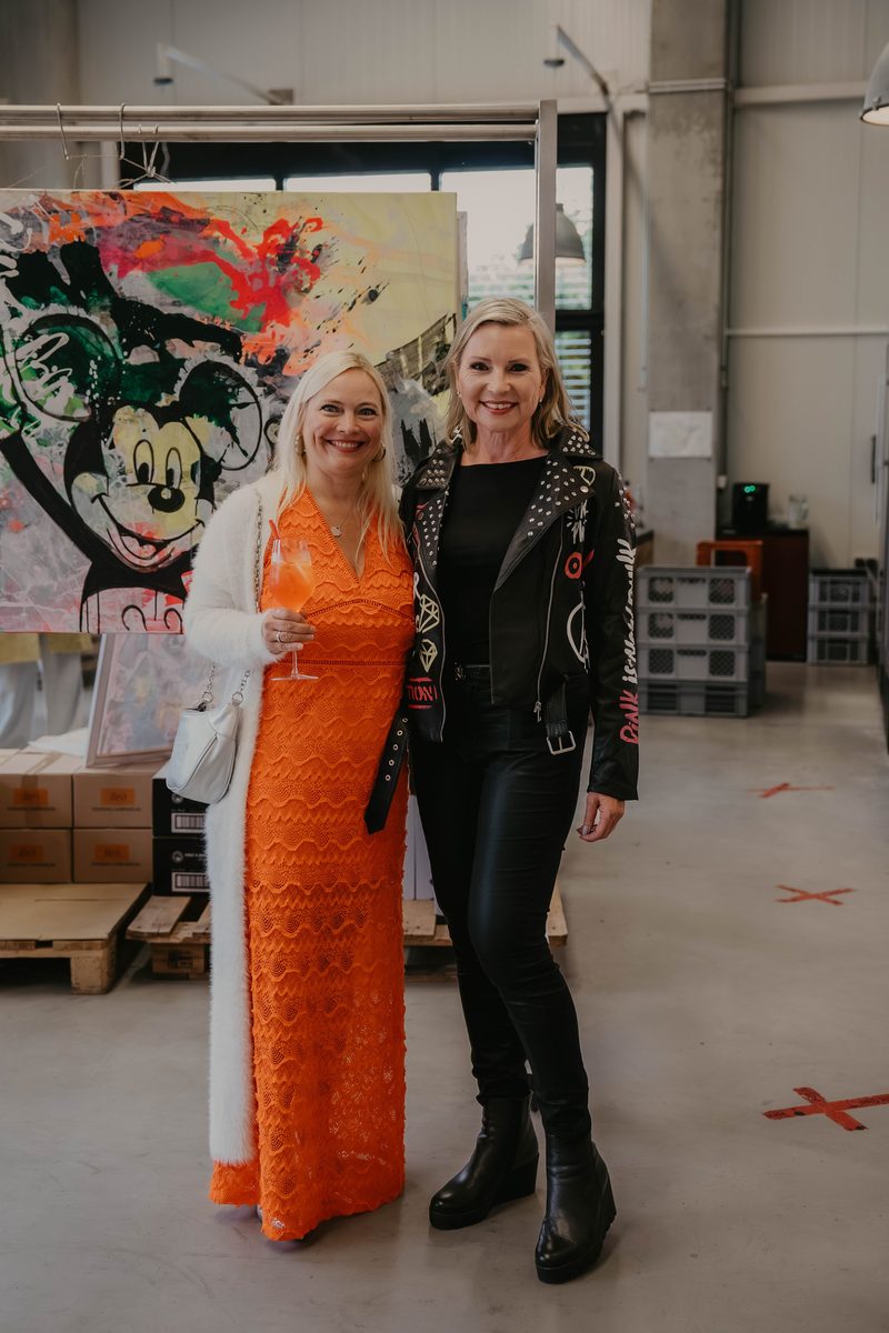 Zwei Frauen posieren gemeinsam vor einem bunten Pop-Art-Gemälde bei der House Art Vernissage
